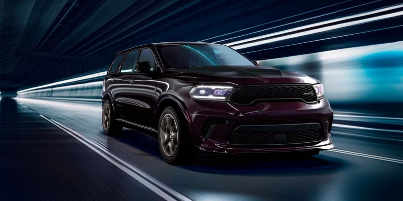 Dark purple SUV with black grille and headlights on, speeding through a dimly lit tunnel.