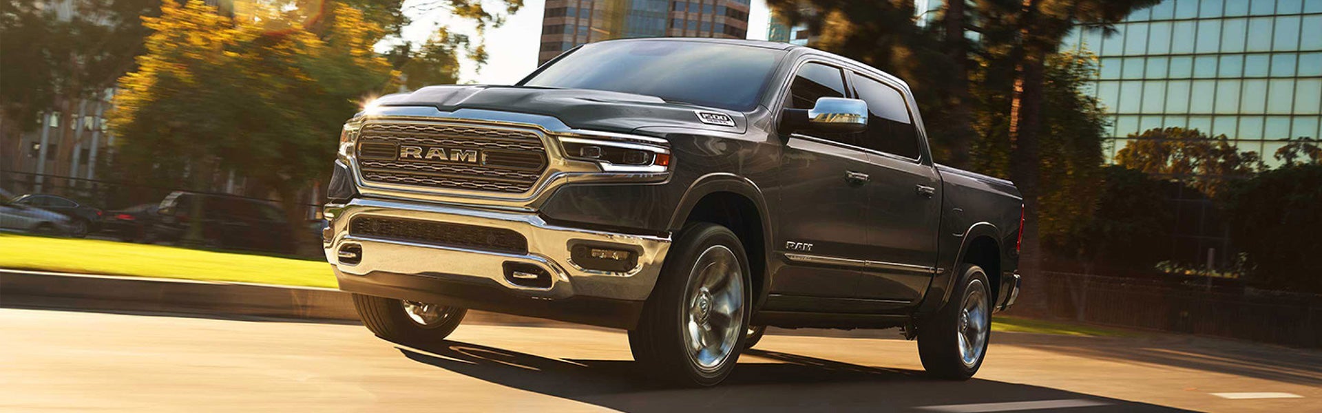 Pre-owned dark gray Ram 1500 truck driving down a city street in late afternoon sun.